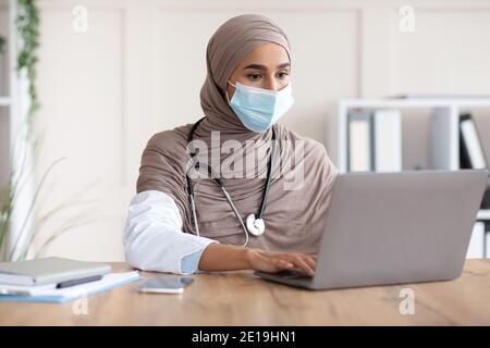 Giovane dottoressa in maschera facciale con laptop Foto Stock