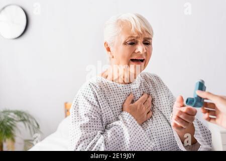 donna anziana che prende l'inalatore dall'infermiere mentre soffre di attacco di asma, in primo piano offuscato Foto Stock