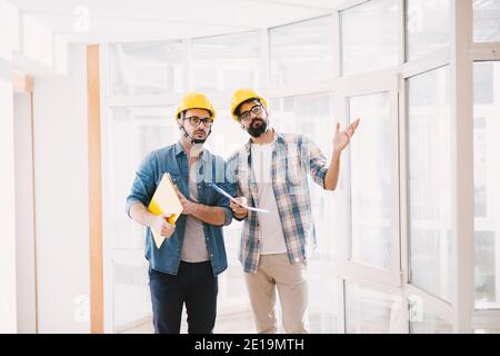 Due giovani ingegneri professionisti con caschi che cercano di risolvere un problema nella pianificazione dei progetti. Foto Stock