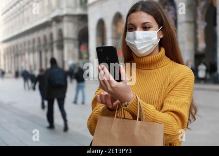 Donna acquirente con maschera chirurgica utilizzando l'app per smartphone in via della città Foto Stock