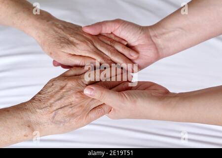 Le mani rughe della donna anziana nei palmi di una giovane donna. Concetto di assistenza e supporto, madre anziana e figlia Foto Stock