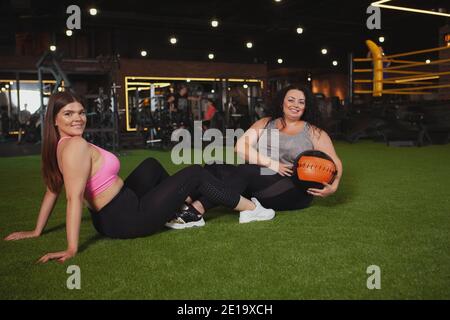 Bella più grande giovane sportivo sorridente alla fotocamera sopra la spalla, godendosi allenarsi con la sua amica in palestra, copia spazio. peso eccessivo tw Foto Stock