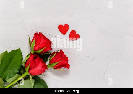 Rose rosse e due cuori di legno su fondo di cemento testurizzato dall'alto. Concetto di amore e di togetherness. Giorno di San Valentino, giorno delle madri. Disposizione piatta Foto Stock