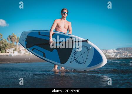 un giovane sportivo pratica il paddle surf sulla spiaggia sotto un cielo blu Foto Stock