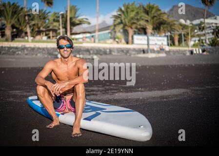 un giovane sportivo pratica il paddle surf sulla spiaggia sotto un cielo blu Foto Stock