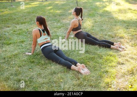 Vista posteriore di due donne che praticano lo yoga all'aperto l'erba Foto Stock