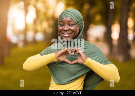 Concetto di amore. Donna musulmana africana sorridente in Hijab mostrando cuore Gesture Foto Stock