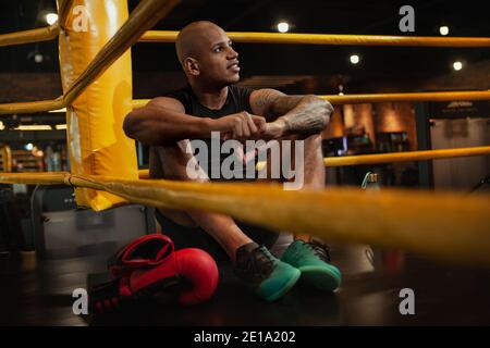 Attraente giovane uomo africano maschio pugilato combattente che riposa dopo aver combattuto in pista di boxe, copia spazio. Bel pugile forte che si concentra prima della sua fi Foto Stock