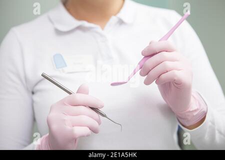 Dentista femminile non riconoscibile che indossa guanti di gomma medica, tenendo in mano gli attrezzi dentali Foto Stock