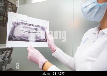 Ripresa tagliata di dentista femminile indossando maschera medica che mostra la mascella scansione a raggi x sulla fotocamera Foto Stock