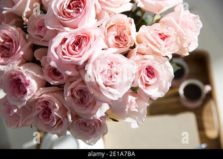 Rosa Bianco Rosa o'hara. Bouquet di rose rosa in vaso di vetro con una teiera bianca e due tazze di cappuccino su un vassoio su un tavolino tra i libri. Foto Stock