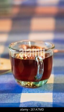 Una deliziosa tazza di tè caldo su una tazza trasparente su un tavolo con una tovaglia blu e bianca Foto Stock