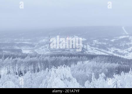 paesaggio invernale - una lontana pianta metallurgica in una valle nel mezzo di foreste innevate in una foschia gelata Foto Stock