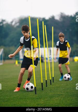 Giovani giocatori di calcio che corrono Slalom e che dribbling con le palle tra i poli di allenamento. Pratica di calcio per ragazzi teenage. Squadra di calcio di livello junior Trai Foto Stock