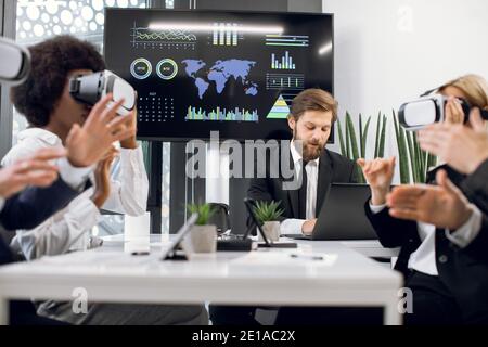 Bell'uomo d'affari di sesso maschile, seduto di fronte allo schermo al plasma, presentando un nuovo progetto al suo team creativo multirazziale, utilizzando la realtà virtuale Foto Stock