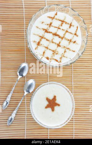 Budino di riso cremoso alla cannella e cucchiai sul tappetino di paglia di bambù come sfondo Foto Stock