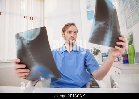 Chirurgo maschile maturo che esamina le scansioni a raggi X di un paziente prima dell'intervento. Medico esperto che esamina le scansioni a raggi X. Foto Stock