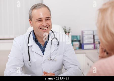 Allegro medico maschio maturo ridendo, parlando con la sua paziente femminile. Medico maschio esperto sorridendo felice al suo paziente anziano Foto Stock