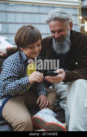 Colpo verticale di un bel ragazzo che insegna il nonno utilizzo di internet su smartphone Foto Stock