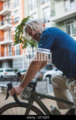 Ritratto verticale troncato di un uomo anziano in bicicletta in città Foto Stock