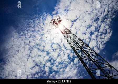 Un'antenna per telecomunicazioni molto alta con un angolo di visione dal basso verso l'alto e una prospettiva evidente dal suolo, con un giorno soleggiato e un cielo blu backg Foto Stock