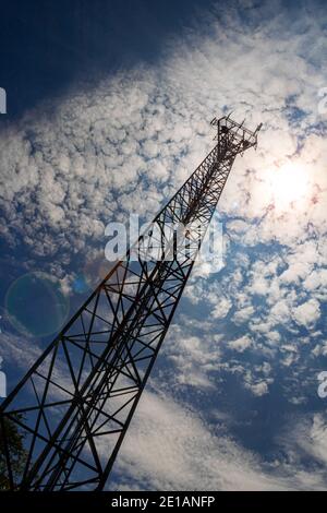 Un'antenna per telecomunicazioni molto alta con un angolo di visione dal basso verso l'alto e una prospettiva evidente dal suolo, con un giorno soleggiato e un cielo blu backg Foto Stock