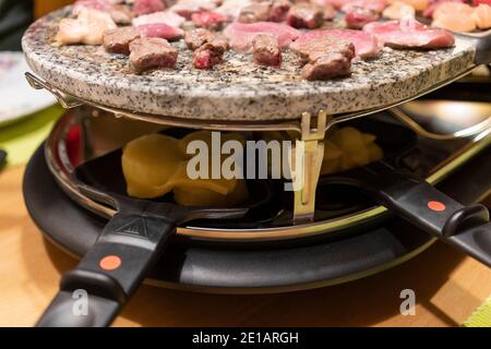 Grigliate di carne e cottura del formaggio in padelle elettriche griglia per raclette da tavolo al centro di un tavolo su Festa di Capodanno in Austria Foto Stock