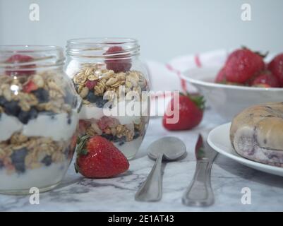 Piatto di parfait yogurt con mirtilli di granola lamponi fragole in un vaso, cucchiaio accanto al vaso e bagel su piatto Foto Stock