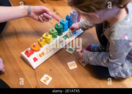 Una figlia imparando a contare con la madre usando un giocattolo educativo. Imparando per prova ed errore, ha messo un numero 7 capovolto per errore Foto Stock