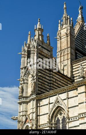 Parte superiore del lato destro della Cattedrale di Siena (XIII secolo) in stile romanico-gotico contro il cielo blu, Toscana, Italia Foto Stock