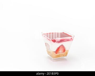 Il primo piano della cheesecake alla fragola in una tazza di plastica trasparente a forma quadrata isolata su sfondo bianco. Foto Stock