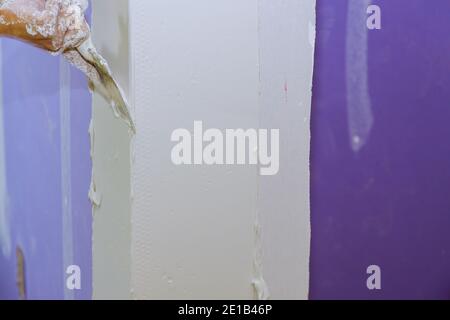 Gesso di lavoro di costruzione con cazzuola a bordo di gesso mette a. rifinitura del tocco nella parete Foto Stock