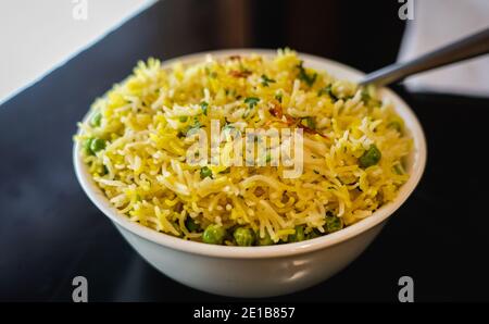 Piselli Pulao, un piatto senza glutine e vegano preparato con riso basmati, piselli verdi, spezie e cipolle fritte, serviti in una ciotola bianca in ceramica. Foto Stock