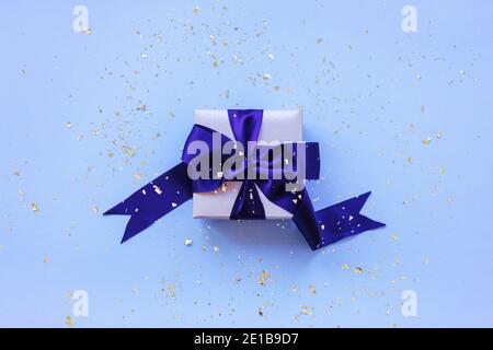 Un regalo in una scatola su sfondo blu festivo con confetti dorati. Vista dall'alto, disposizione piatta. Foto Stock