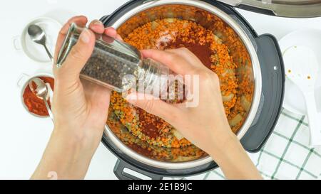 Ricetta per zuppa di lenticchie, cucinando usando un moderno fornello multiplo. Donna aggiunge pepe nero in pentola Foto Stock