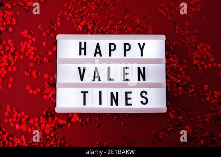 Lightbox con parole per Happy Valentines su rosso lucido confetti pailled sfondo con piume. San Valentino e Natale di fondo . Hol Foto Stock