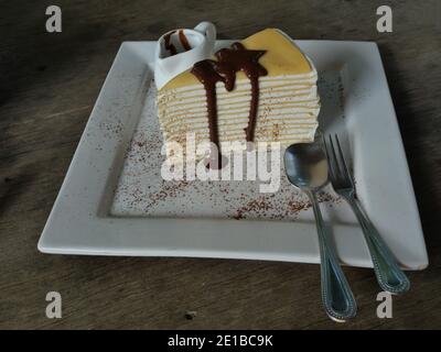 Torta crepe con sciroppo di cioccolato e polvere di cocco in un piatto bianco su un tavolo di legno marrone, torta fatta da pasta sottile di crosta diversi strati di strato Foto Stock