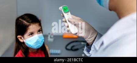 Medico femminile che guarda il termometro a infrarossi dopo aver preso tempe Foto Stock