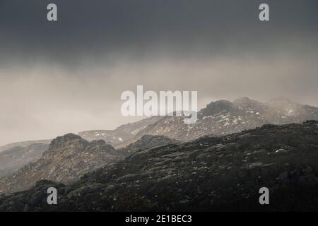 Paesaggio montano con capes nevosi in una giornata piovosa, come la luce entra attraverso le nuvole Foto Stock