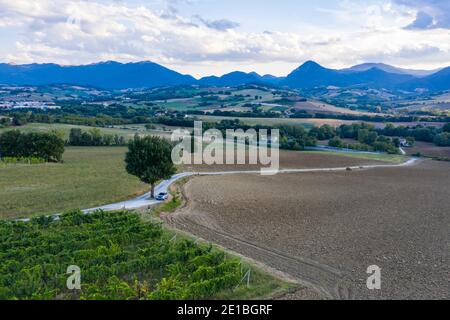 Vista aerea di una STRADA 'S' nella campagna fuori Fabriano, Italia. Un albero solitario è in piedi sulla strada e una macchina è parcheggiata sotto di essa. Foto Stock