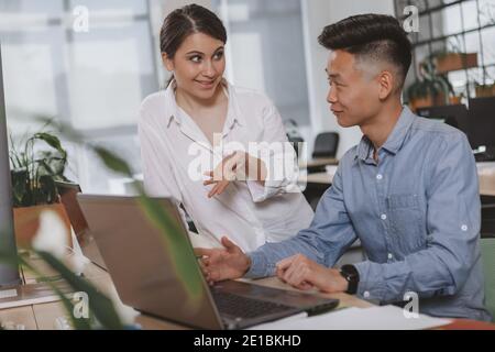 Giovani uomini d'affari che parlano con gioia mentre lavorano a un progetto usando un laptop. Allegra donna d'affari sorridente, parlando di affari con il suo maschio colle Foto Stock