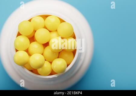 Le vitamine sono gialle in un vaso bianco su sfondo blu-blu. La vitamina C del dragee il concetto di salute. Foto Stock