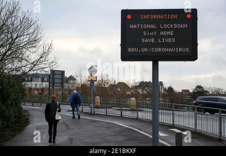 La gente passa accanto a un cartello informativo che informa la gente circa il blocco nazionale a Staines-upon-Thames in Surrey. Il primo ministro Boris Johnson ha ordinato un nuovo blocco nazionale per l'Inghilterra, il che significa che le persone potranno lasciare le proprie case solo per motivi limitati, con misure che dovrebbero rimanere in vigore fino a metà febbraio. Foto Stock