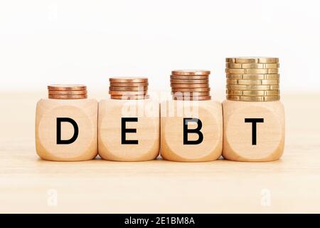 Concetto di debito. Blocchi di legno con testo e monete su tavolo di legno. Copia sfondo bianco spazio Foto Stock