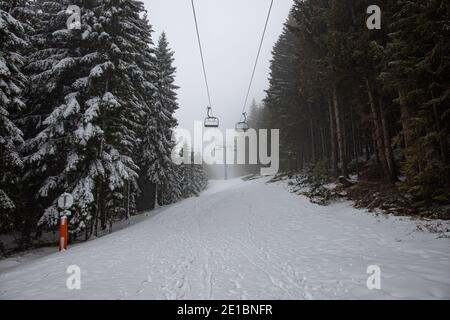 Empty Ski Lift su un paesaggio invernale innevato, con montagne innevate e grandi pini e abeti, nella nebbia. La seggiovia non ha persone Foto Stock