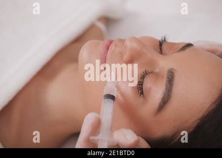 Donna attraente che ottiene iniezioni facciali alla clinica di cosmetologia. Donna attraente che riceve iniezioni di acido ialuronico da dermatologo professionista. Foto Stock