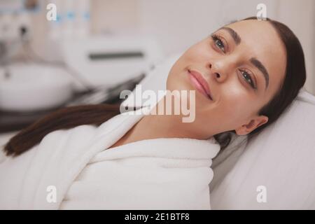 Primo piano di una bella donna felice e sana, sorridente, guardando via gioiosamente, rilassante al centro termale. Splendida giovane donna con pelle impeccabile sana re Foto Stock