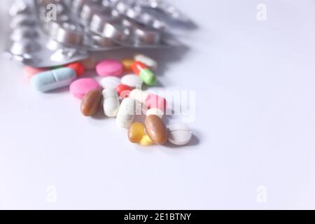 Primo piano di molte pillole colorate e capsule che si versano sopra bianco Foto Stock