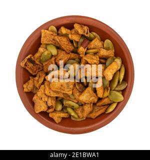 Vista dall'alto di una piccola ciotola piena di semi di zucca tostati organici con pezzi di mela disidratati isolati su sfondo bianco. Foto Stock