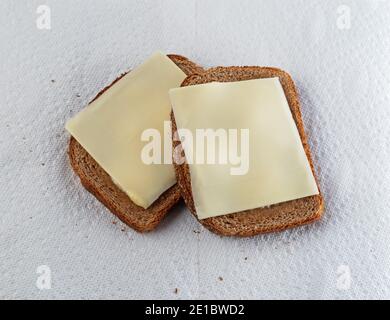Vista dall'alto di due fette di pane di grano leggermente tostato con margarina e formaggio a fette su asciugamani di carta bianca con luce naturale. Foto Stock